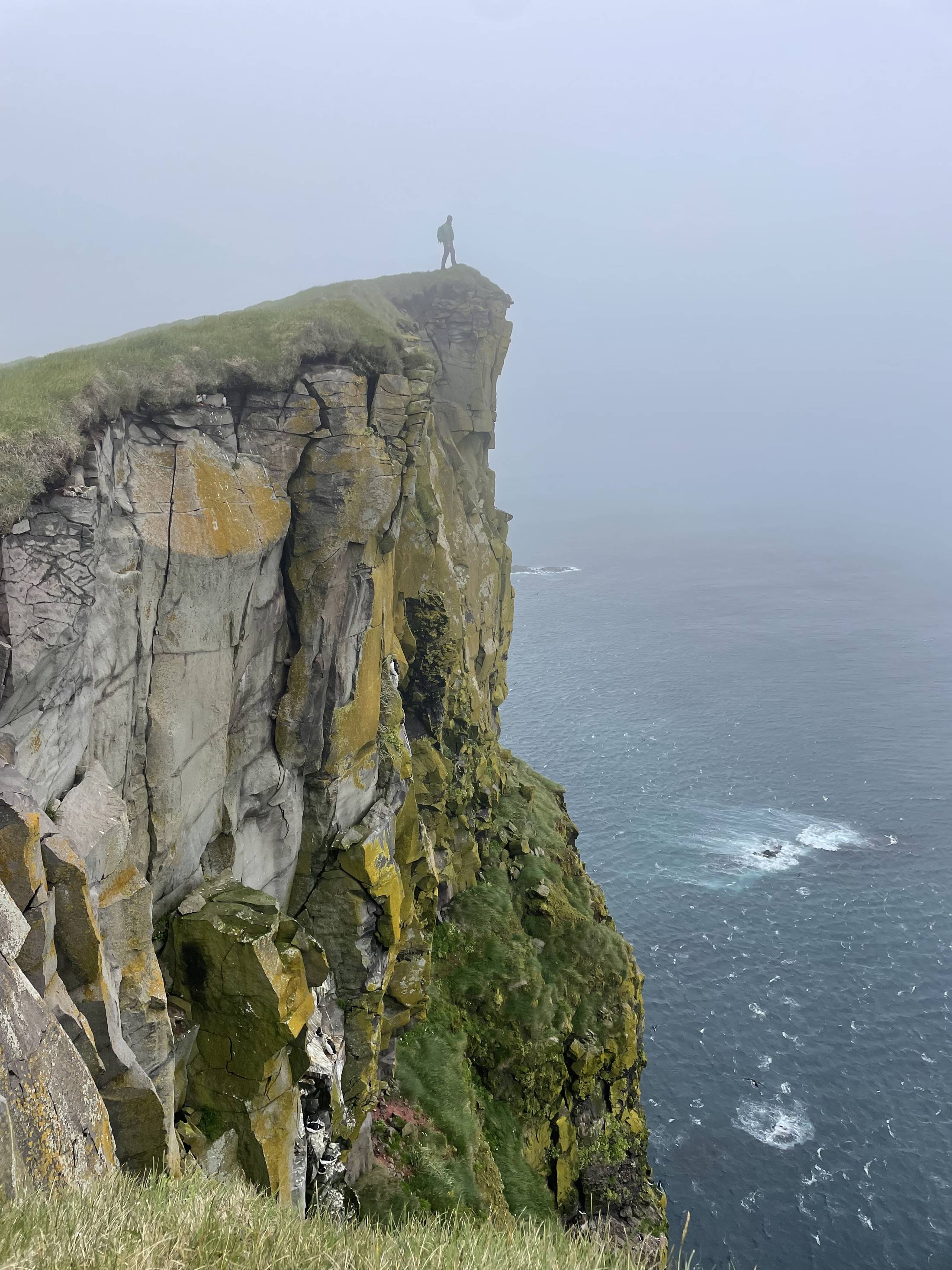 A hiker stands alone on the edge of a fog-wrapped sea cliff